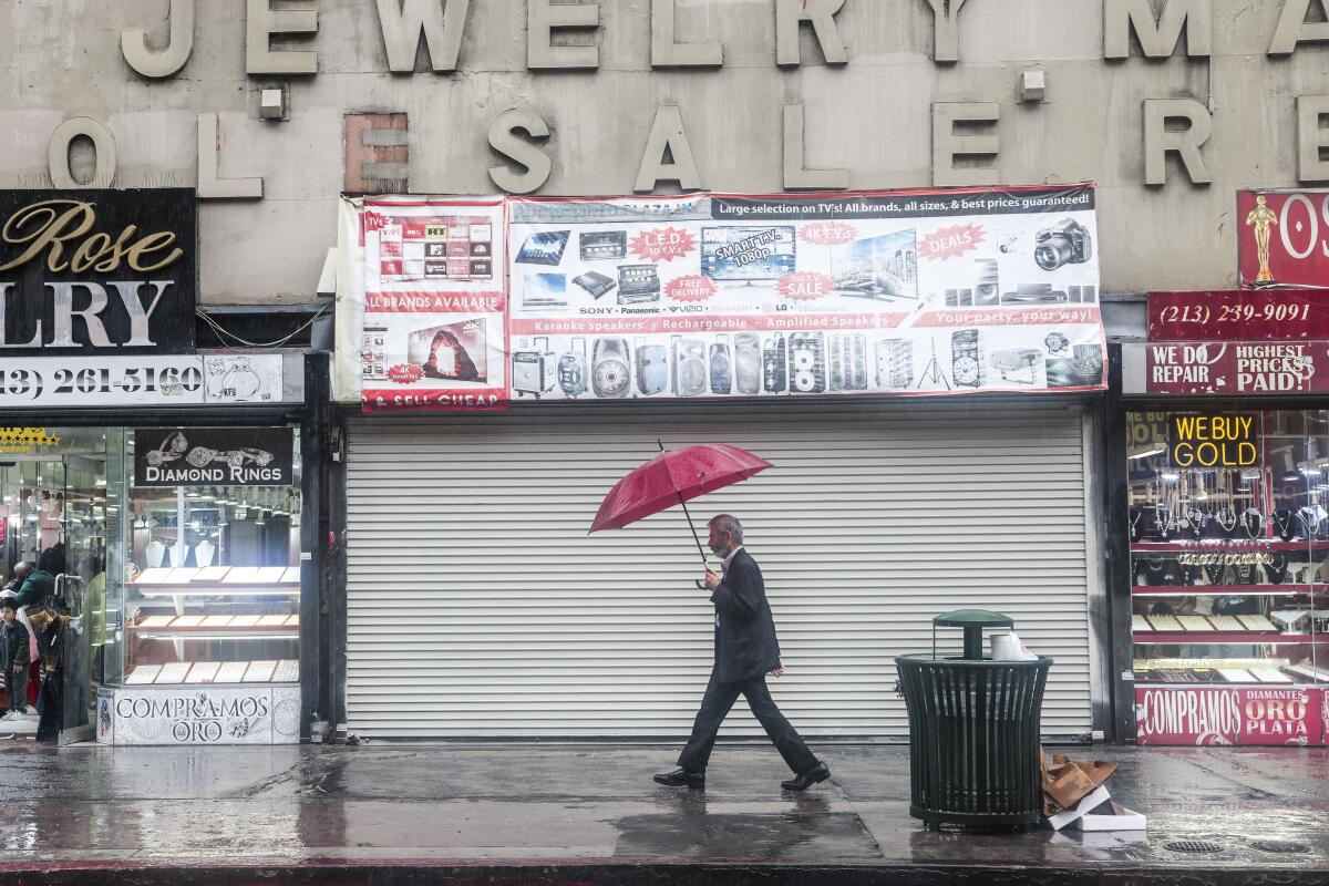 A person walks under an umbrella during Tropical Storm Hilary while downtown in Los Angeles. 