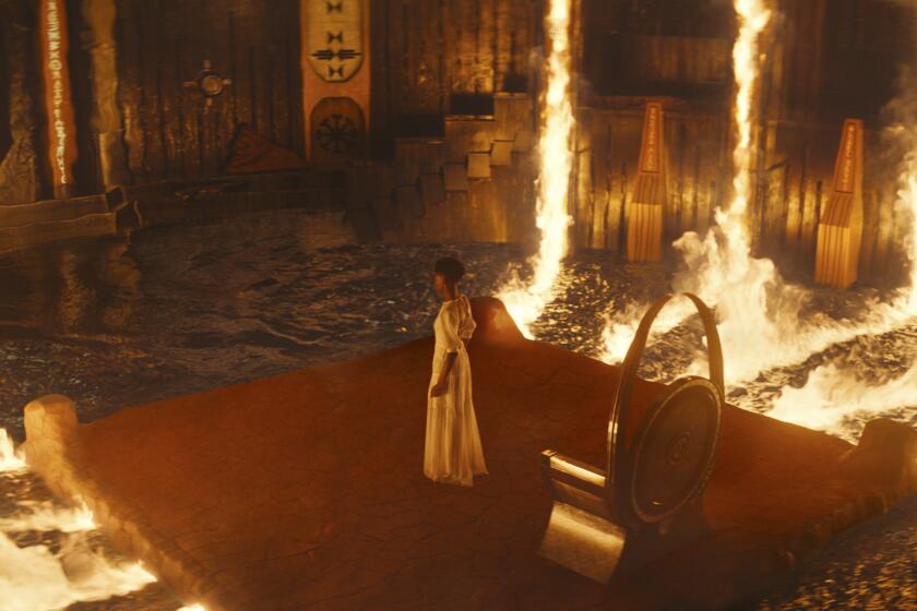 W woman in a white dress stands on platform surrounded in fire