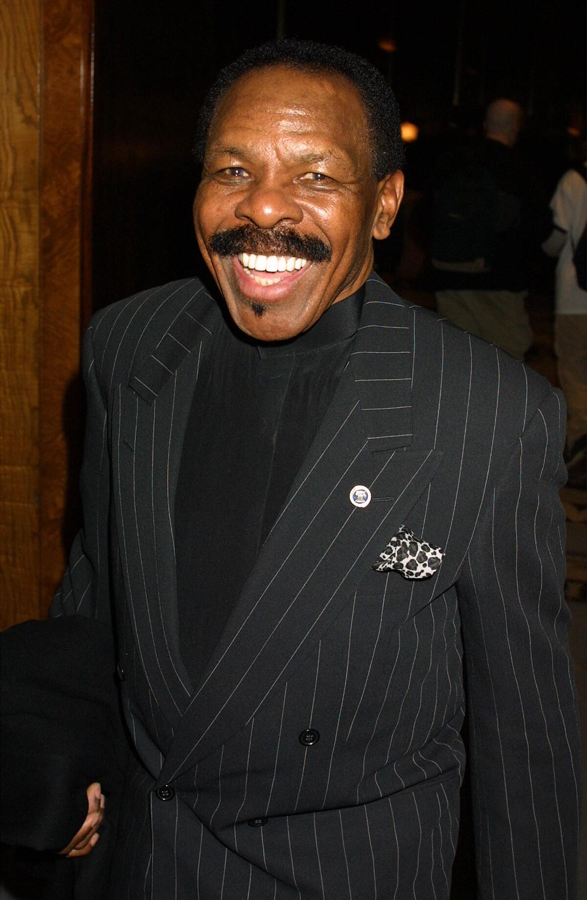 Singer Lloyd Price smiles while wearing a pinstripe jacket with a pin on his lapel.