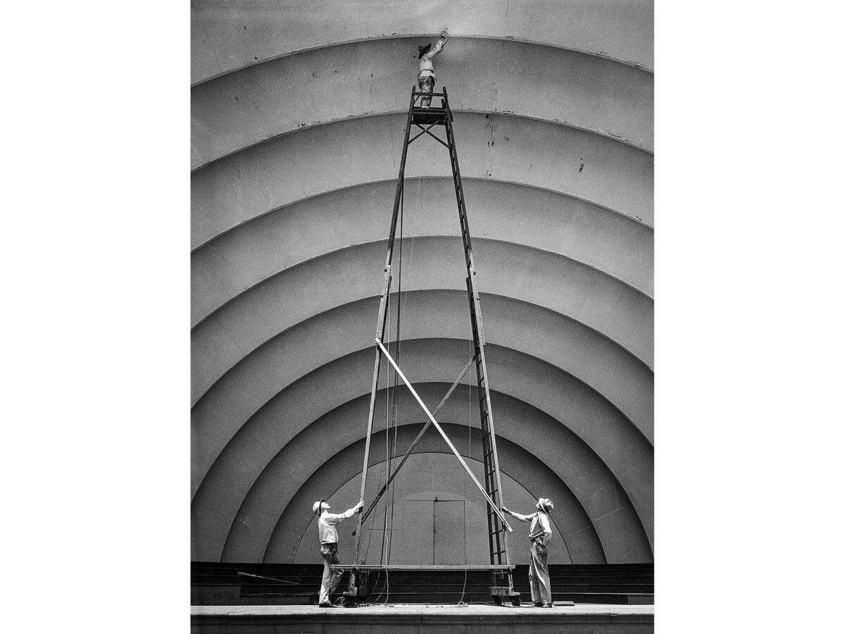 July 5, 1935: Two workers steady a ladder as Martin Sipma uses a spray gun to paint the top of the Hollywood Bowl shell.