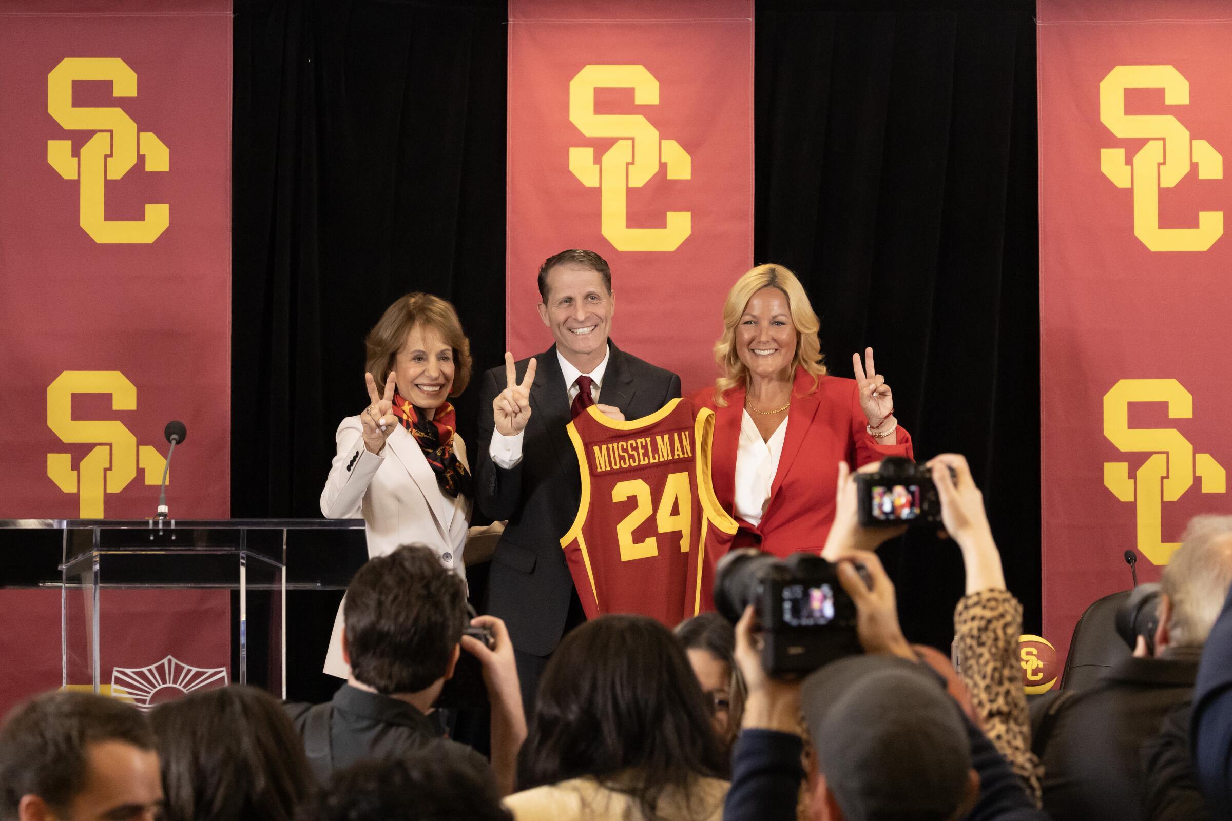 Eric Musselman holds a USC jersey while standing between USC president Carol Folt and athletic director Jennifer Cohen.