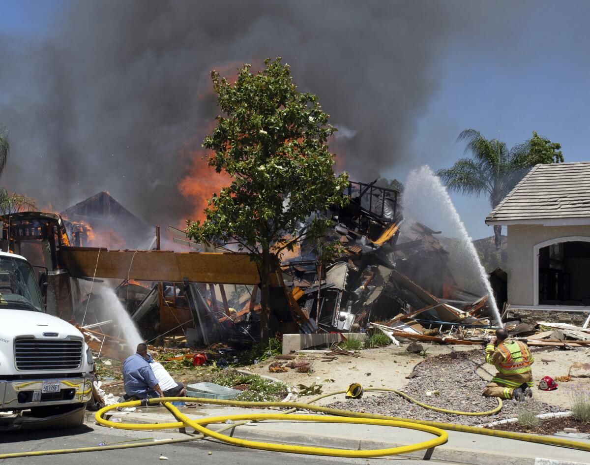 A firefighter and civilians train hoses on a burning home after a gas line explosion destroyed the house in Murrieta, Calif.