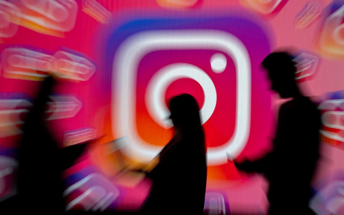 Shadows of three figures in front of blurry Instagram logos on a screen.