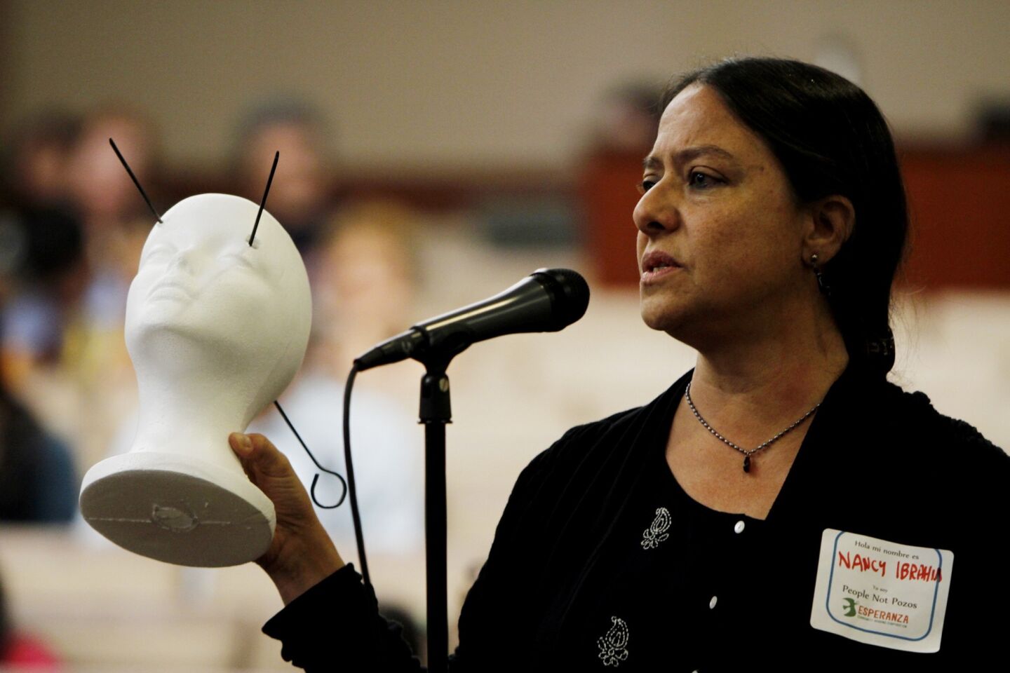 Nancy Halpern Ibrahim, executive director of Esperanza Community Housing Corp., speaks during a town hall meeting concerning fumes from a South Los Angeles oil field. She holds a model that she says depicts some of the symptoms, including headaches and nose bleeds, that people living near the field are experiencing.