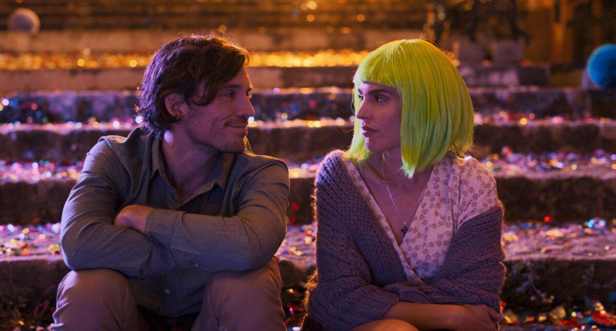 A smiling man and a woman wearing a lime green wig look at each other while sitting on steps.