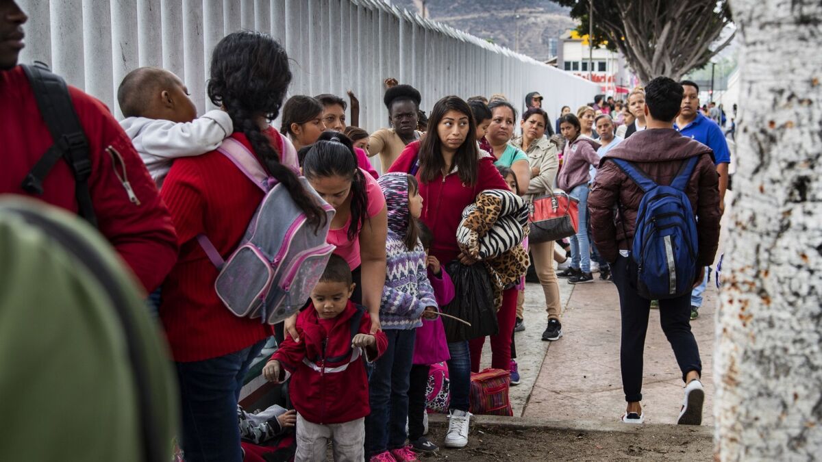 Asylum-seeking immigrants line up at a border fence in Tijuana, Mexico.