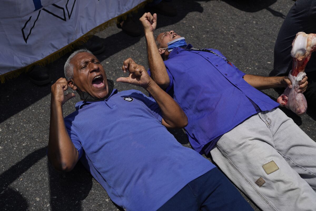 People lie down on a street as they scream demanding better salaries for workers, pensioners and retirees, during a protest in Caracas, Venezuela, Wednesday, April 6, 2022. (AP Photo/Ariana Cubillos)