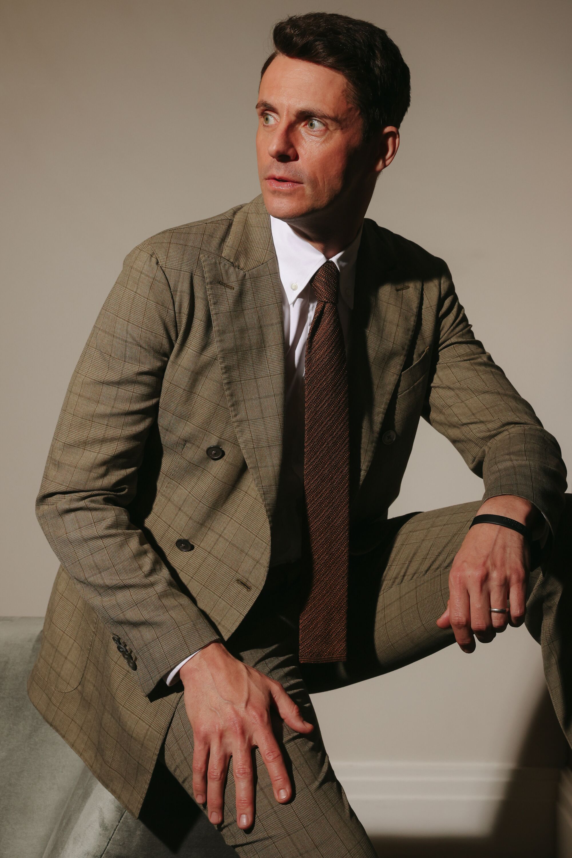 A seated man in a brown suit and darker brown tie.