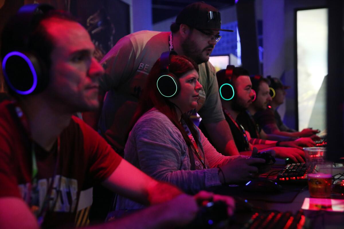 Roberto Garcia-Lago, top, looks over Laura Goodman's shoulder, center left, while she plays “Doom Eternal” at the Bethesda booth during E3.