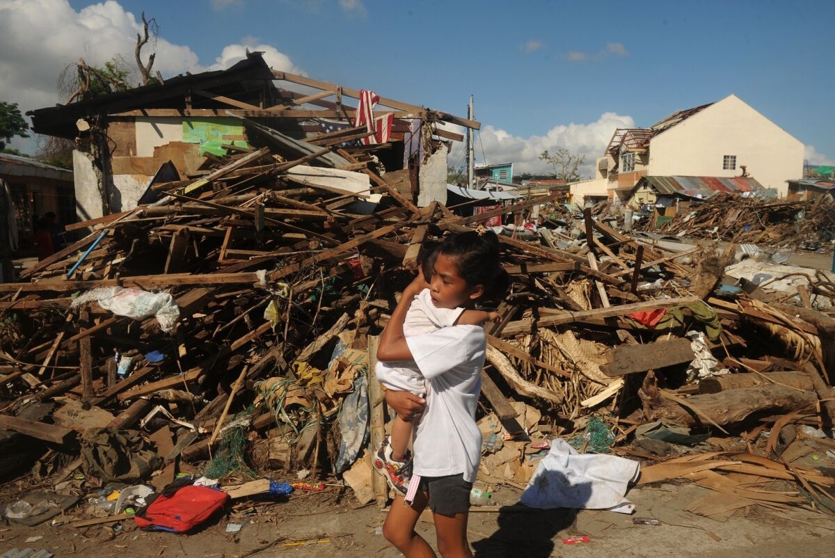 A girl carries a baby past debris in the Philippine city of Tacloban, which was devastated by Typhoon Haiyan.