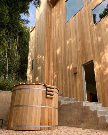 A hot tub ringed in wood like a barrel that matches the exterior woodwork on a house. 