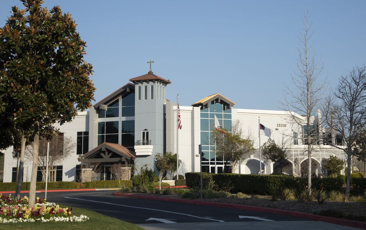 The exterior of a large building that has an American flag out front and a cross on top.