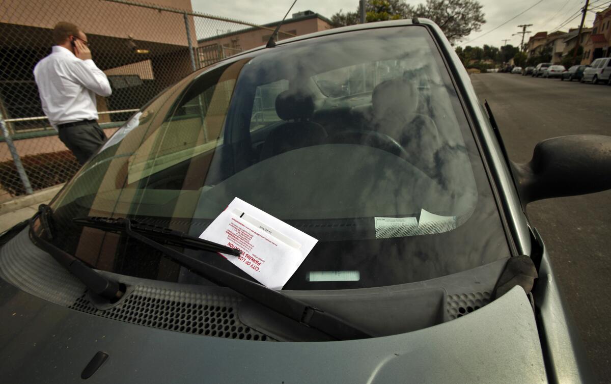 A man is on the phone next to a car with a ticket on its windshield.