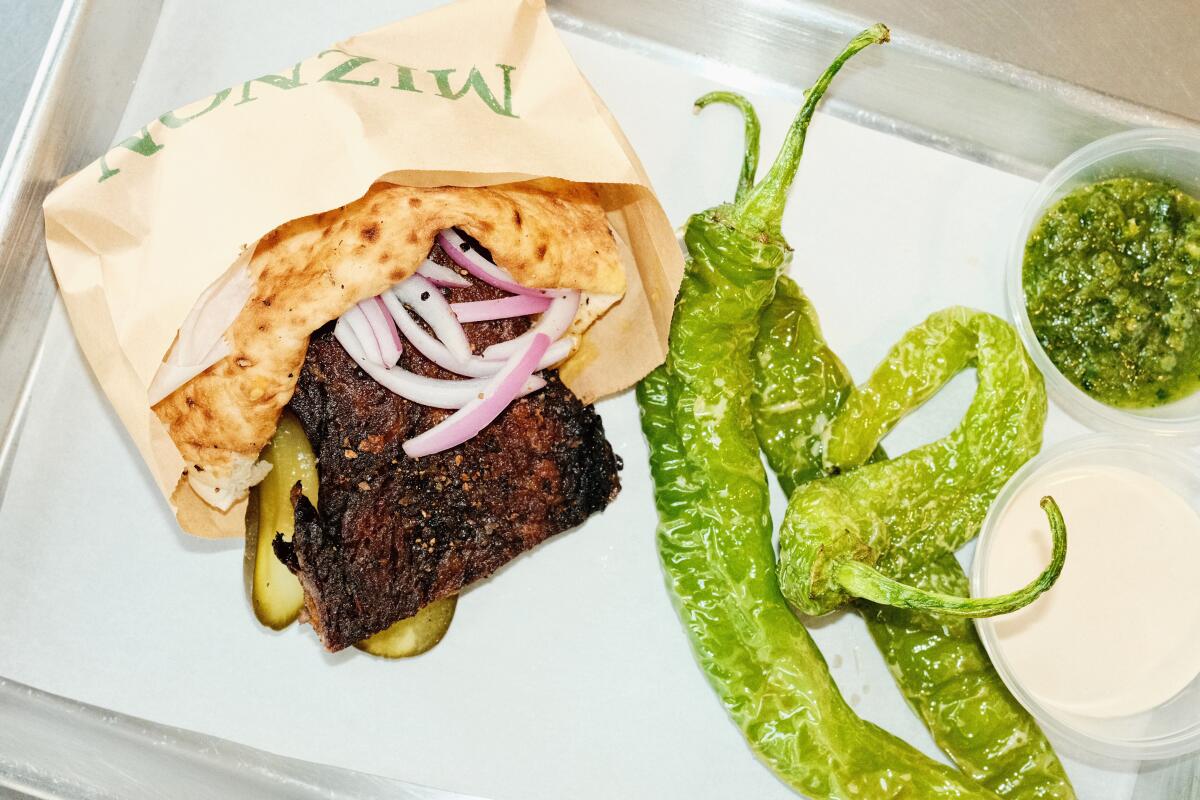 A steak pita with brisket, onions, mustard and pickles on a silver tray with green peppers at Miznon in Grand Central Market.