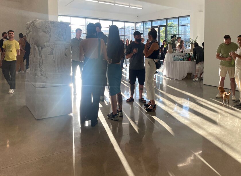 People stand around a sculpture in a sunlit gallery.