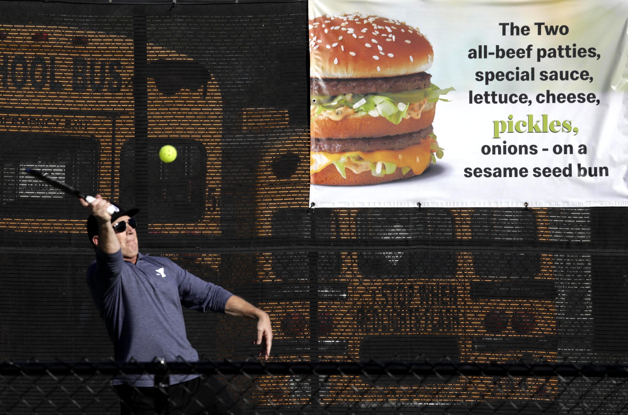 A pickleball player hits the ball in front of a sign showing a Big Mac