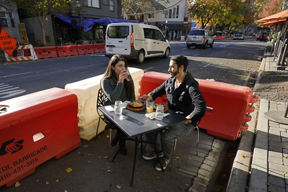 FILE - In this Nov. 20. 2020, file photo, Ranim Abaad and Joey Bettencourt, right, have lunch outdoors at the RIND in Sacramento, Calif. California Gov. Gavin Newsom signed three bills, Friday Oct. 8, 2021 to help bars and restaurants recover from the coronavirus pandemic. Two of the three bills extend outdoor dining permits and alcohol sales at the pandemic-era parklets for a year after the state of emergency ends, giving businesses time to seek permission for permanent approval. The third allows restaurants, bars, breweries and wineries that sell food to continue offering to-go alcoholic beverages with food orders through Dec. 31, 2026. (AP Photo/Rich Pedroncelli, File)