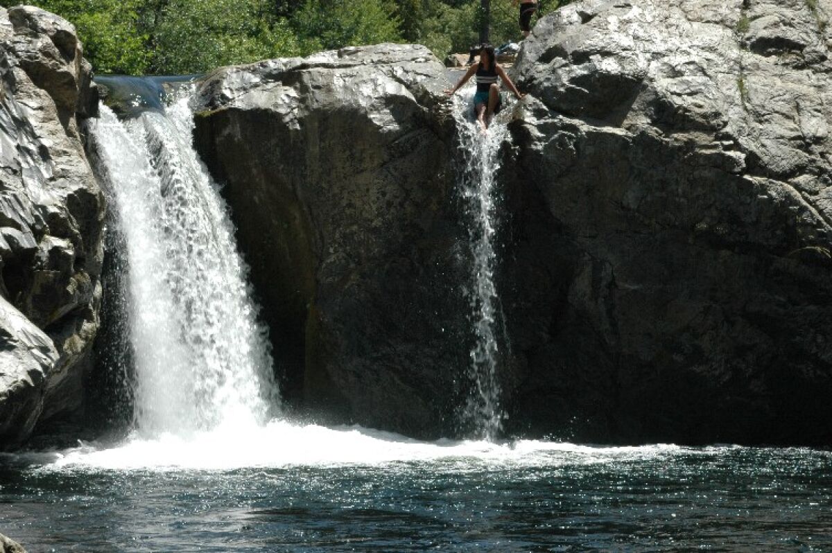 A person sits atop a boulder next to a waterfall splashing into a pool below.