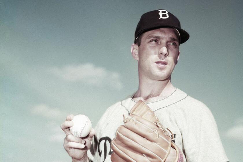 Brooklyn Dodgers pitcher Carl Erskine holds the ball and looks across the field.