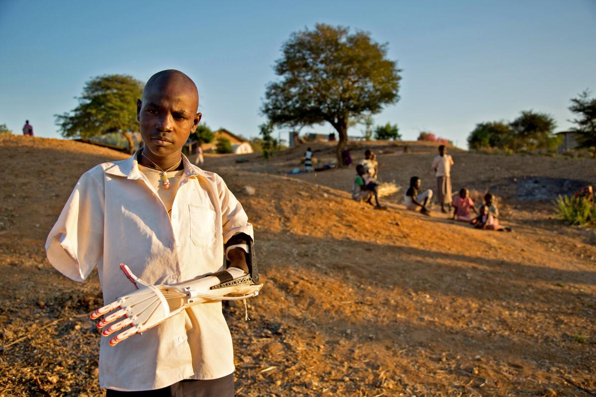 Daniel Omar, standing outside a hospital in Gidel, Sudan, wears a prosthetic arm made with a 3-D printer supplied by Not Impossible, a Venice group that helps people overcome physical limitations through technology.