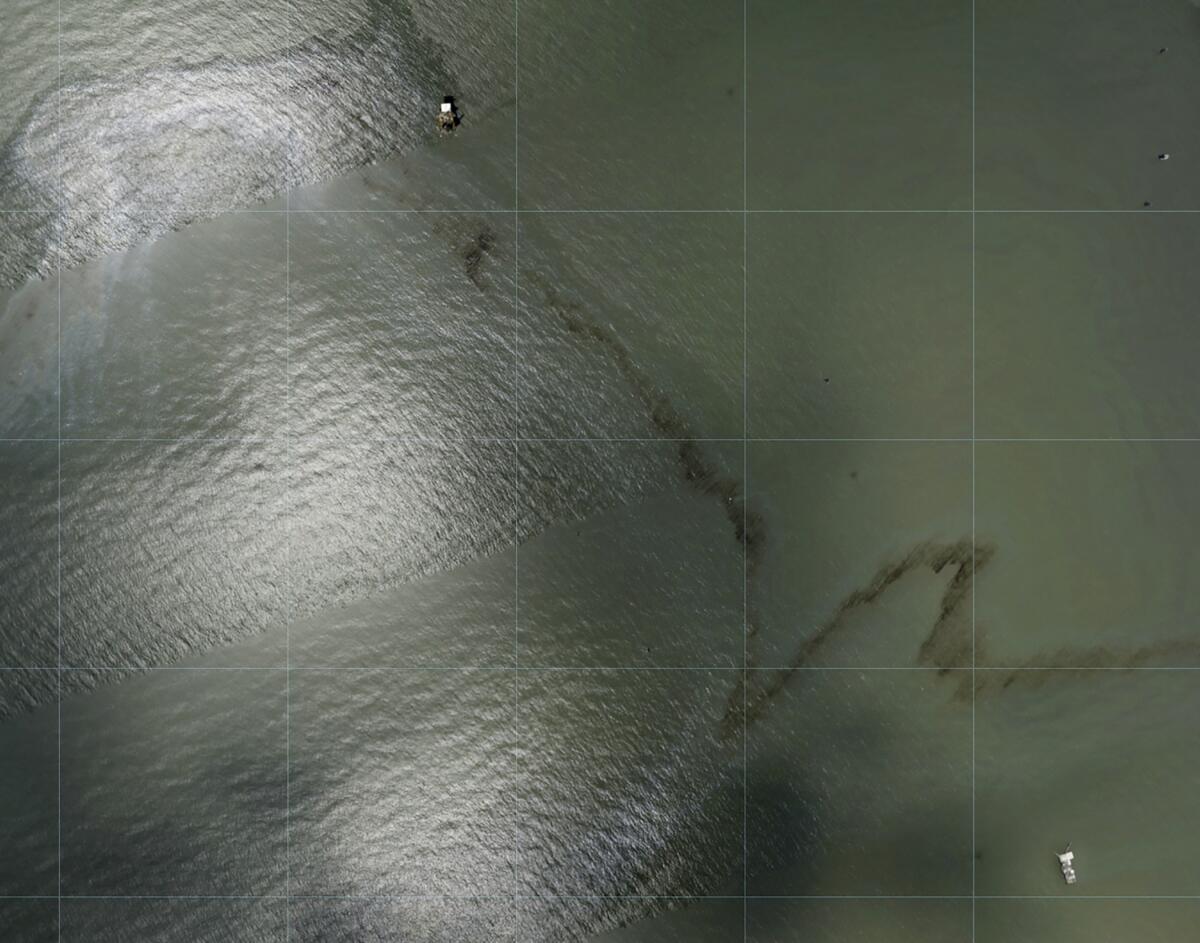 Overhead view of a miles long black slick floating in the Gulf of Mexico near a large rig.