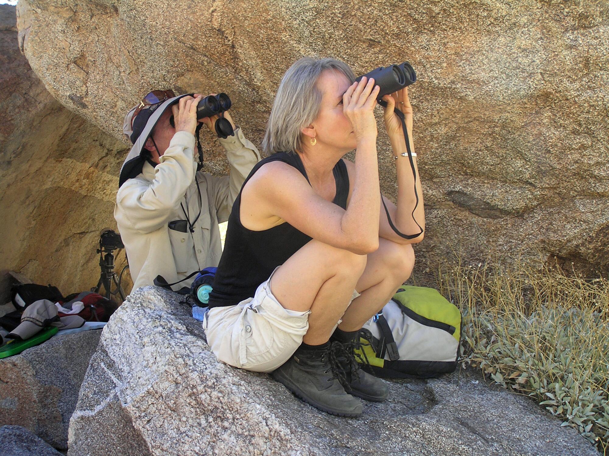Phillip Roullard and Denise Zuranski look through binoculars amid rocks in the shade.