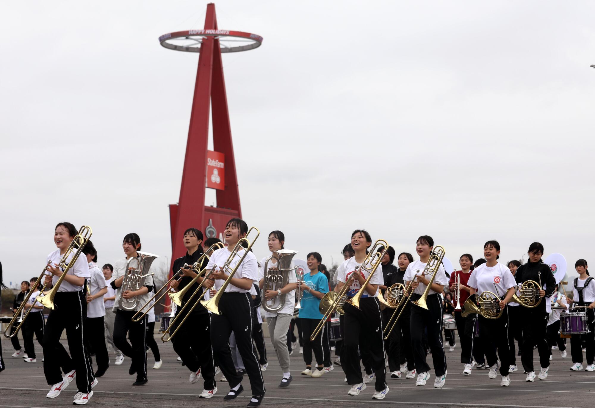 A group of people with musical instruments march in a stadium parking lot.
