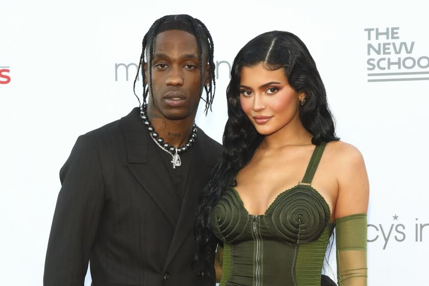 Travis Scott and Kylie Jenner posing in a black suit and green dress, respectively