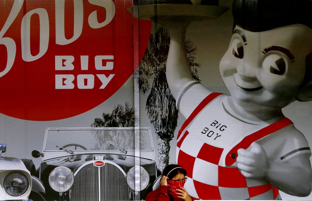 2020 年，一位女士在进入伯班克最初的 Bob's Big Boy 餐厅之前调整了她脸上的头巾。 