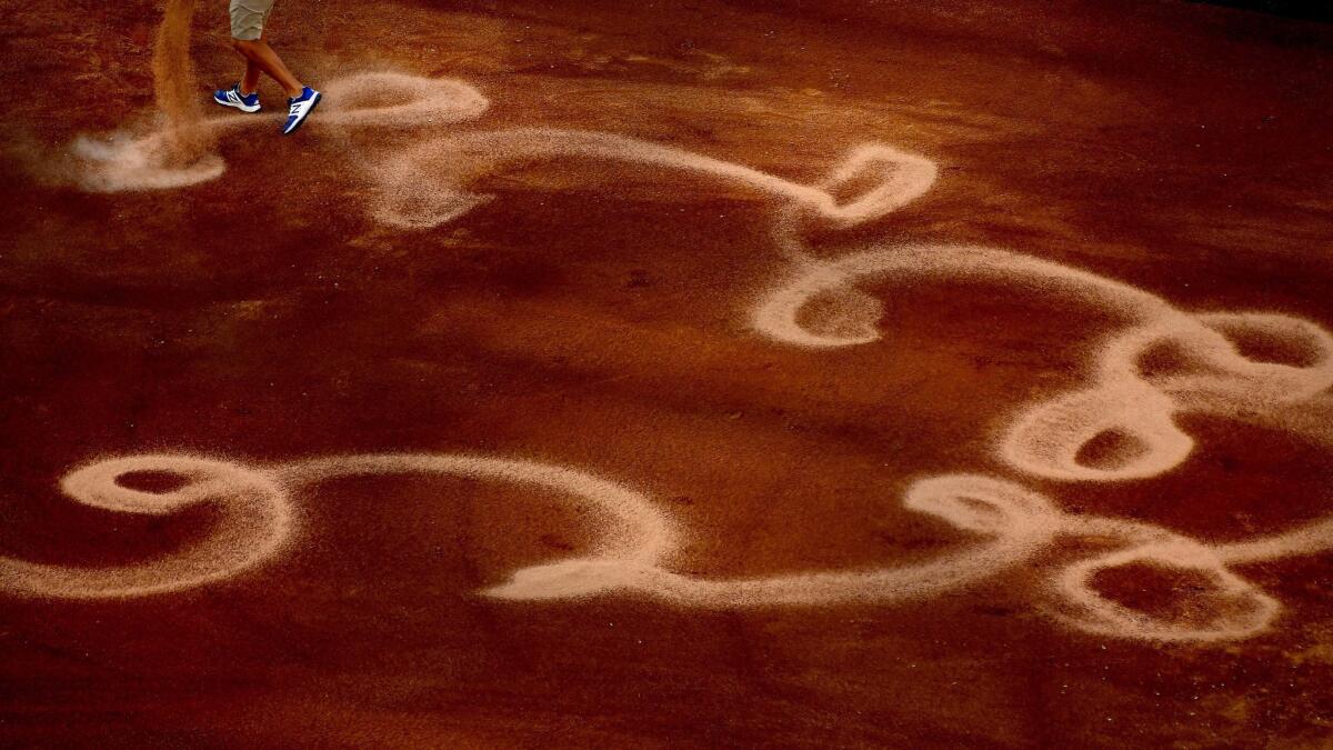 A member of the ground crew pours sand on the infield before a game against the Rockies at Dodger Stadium.