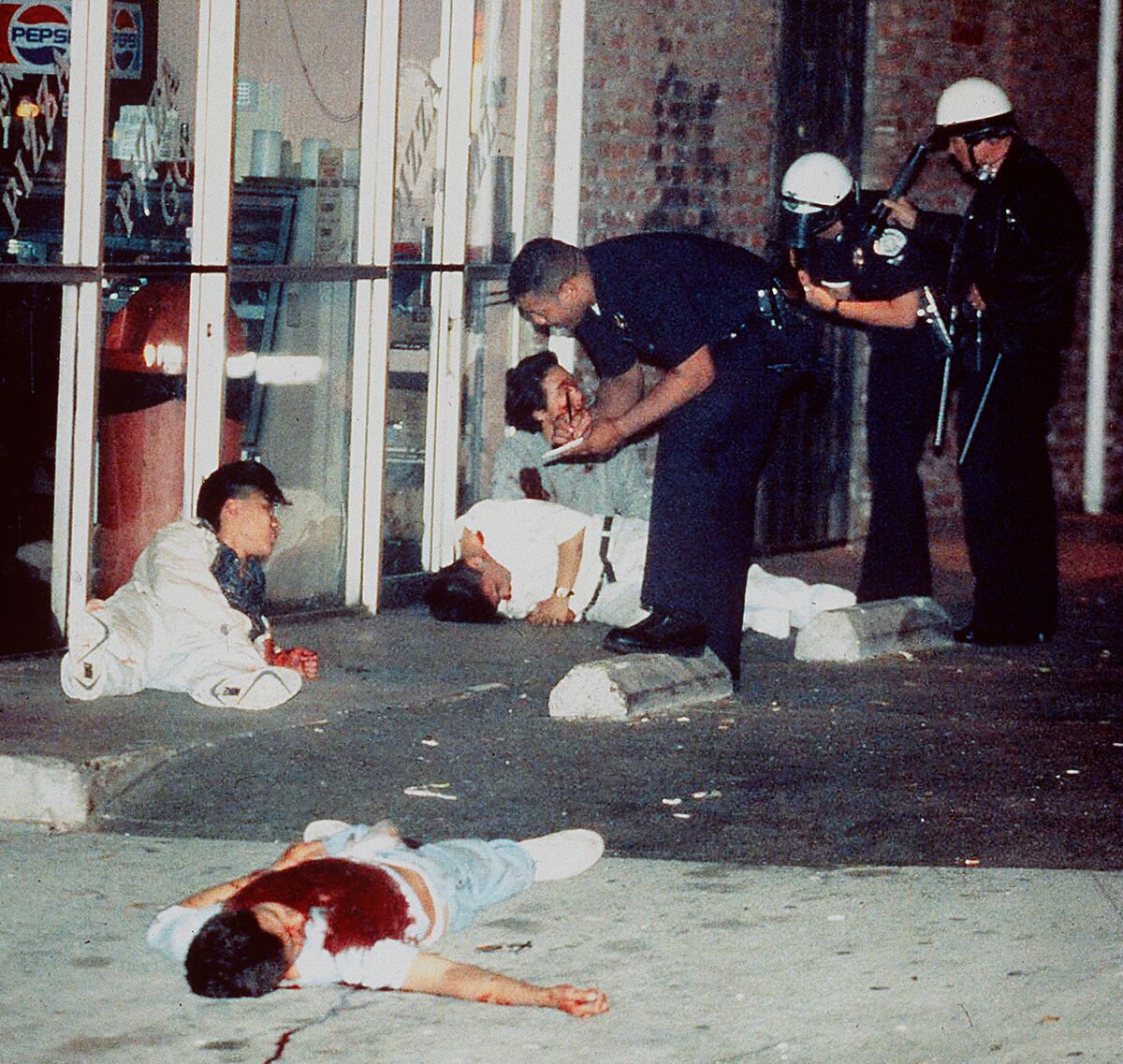 Four bloody men lie on the ground as three policemen talk to them.