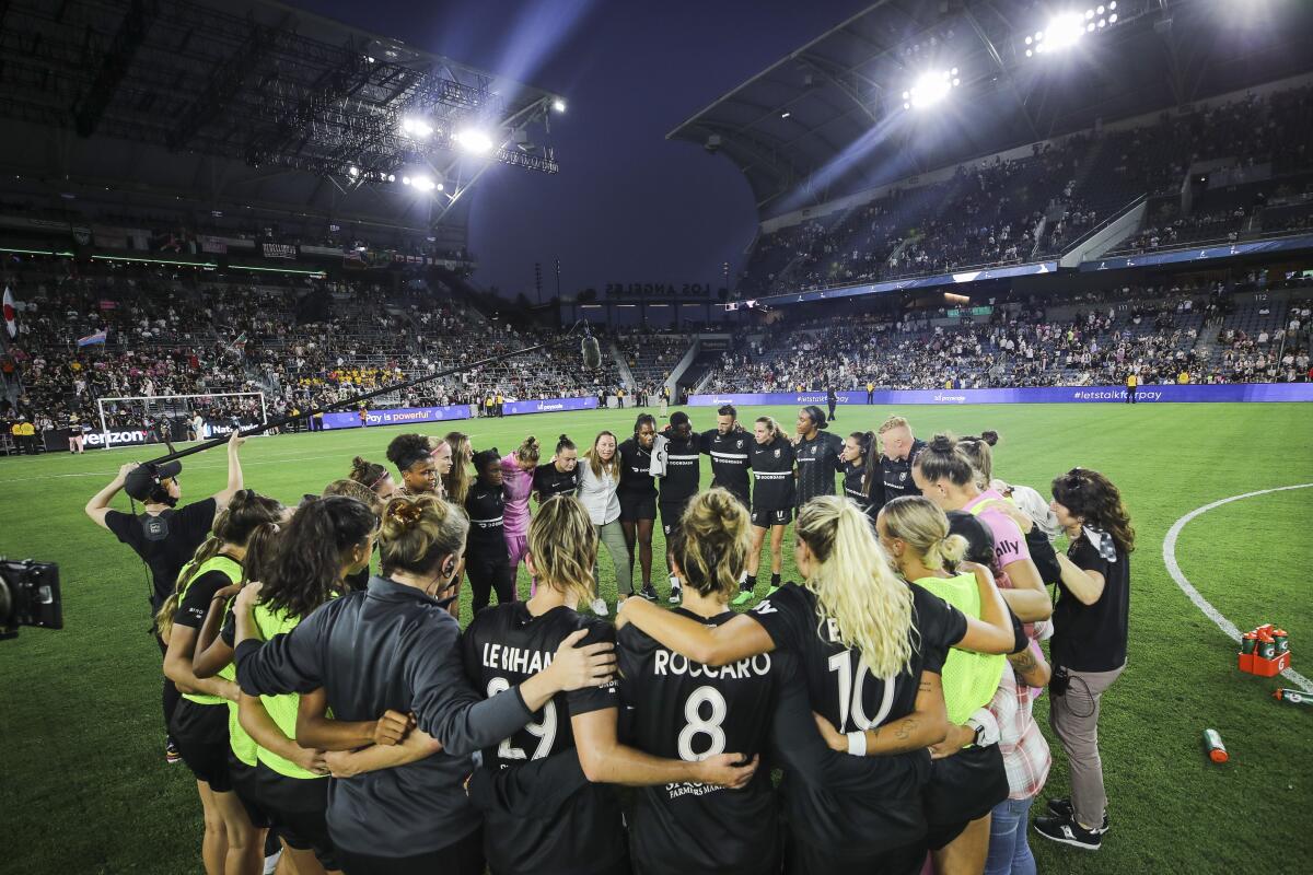 Angel City FC players and coaches huddles together on the field after a game.