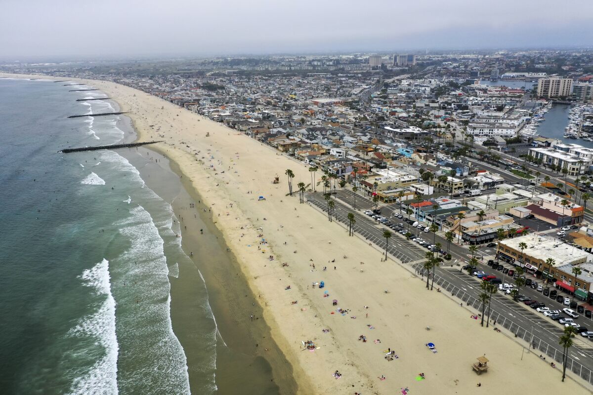 An aerial view of people on a beach lined with homes and parking lots