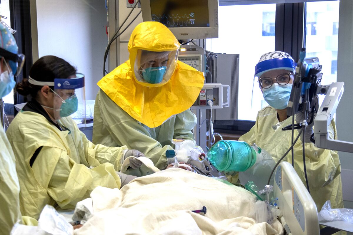 A medical team in face shields, masks and other protective gear treats a patient on a hospital bed.