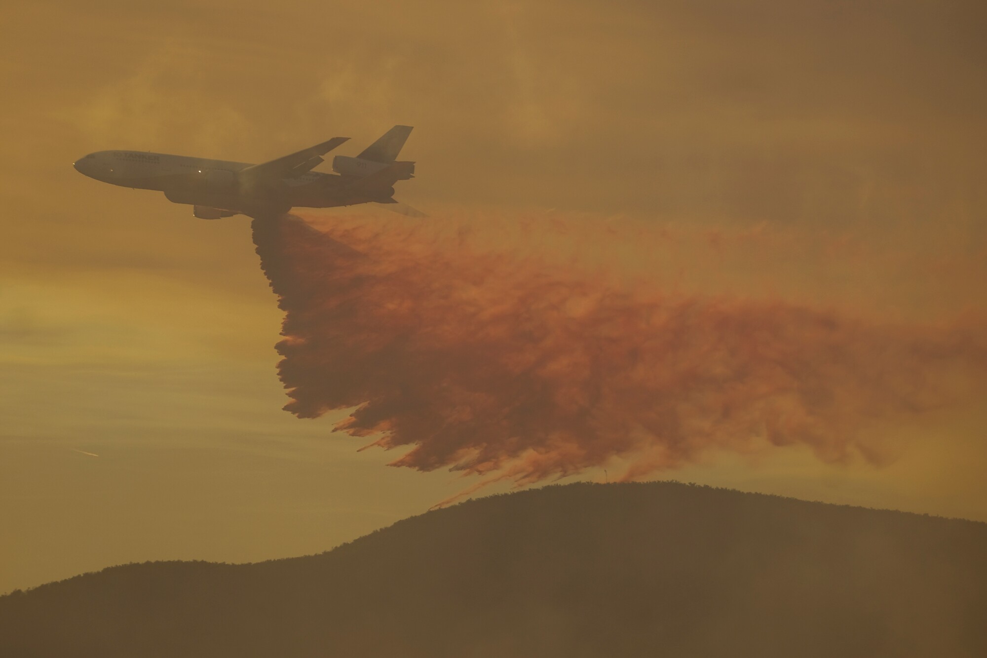 Enveloped in smoke, a tanker plane drops a retarder on the Fire Road in Castaic.