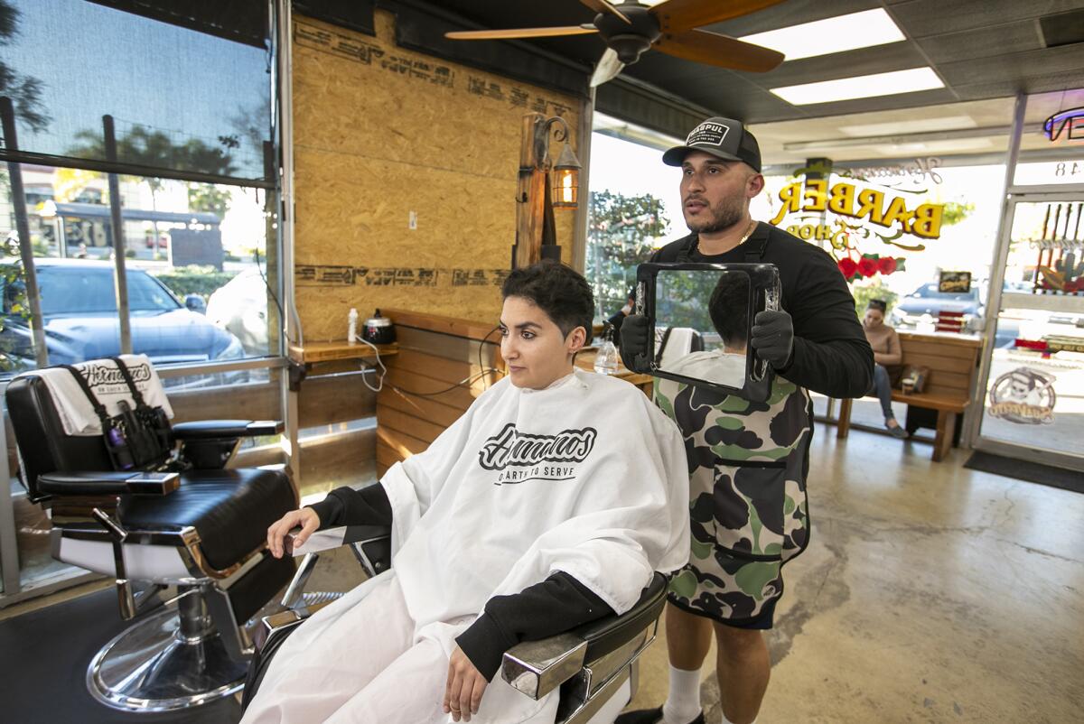  Isaac Garcia shows Jana Baervoets after haircut at at Hermanos Barbershop on Monday in Huntington Beach.