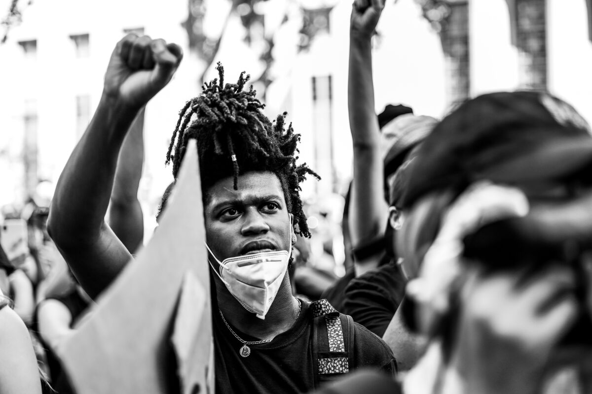 An unidentified Black man sits with his fist raised, a protective mask on his chin, at a June 3, 2020, protest.