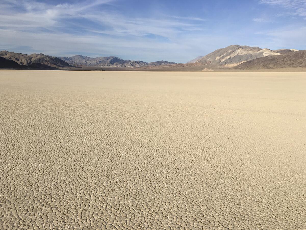 A barren cracked desert landscape under blue skies with mountains in the distance.