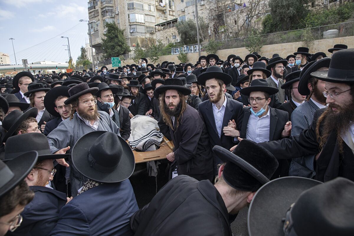 A casket is carried amid a dense crowd of people in ultra-Orthodox garb.