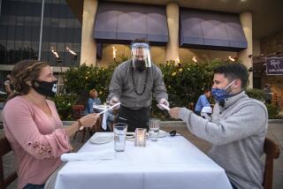 WOODLAND HILLS, CA -JULY 17, 2020: Jason Ruckart, center, a managing partner at Roy's Restaurant in Woodland Hills, hands chopsticks to customers Nicole Lehning, and her husband Kyle, as they dine outdoors. The Lehning's, visiting from Seattle, Washington, said they are on their honeymoon. Fleming's Prime Steakhouse and Roy's Restaurant, located next to each other, converted the valet parking area into outdoor dining. Due to the coronavirus, the restaurants are only allowed to have outdoor dining and takeout as a safety precaution. Valet parking is also not allowed, only self-parking. (Mel Melcon / Los Angeles Times)