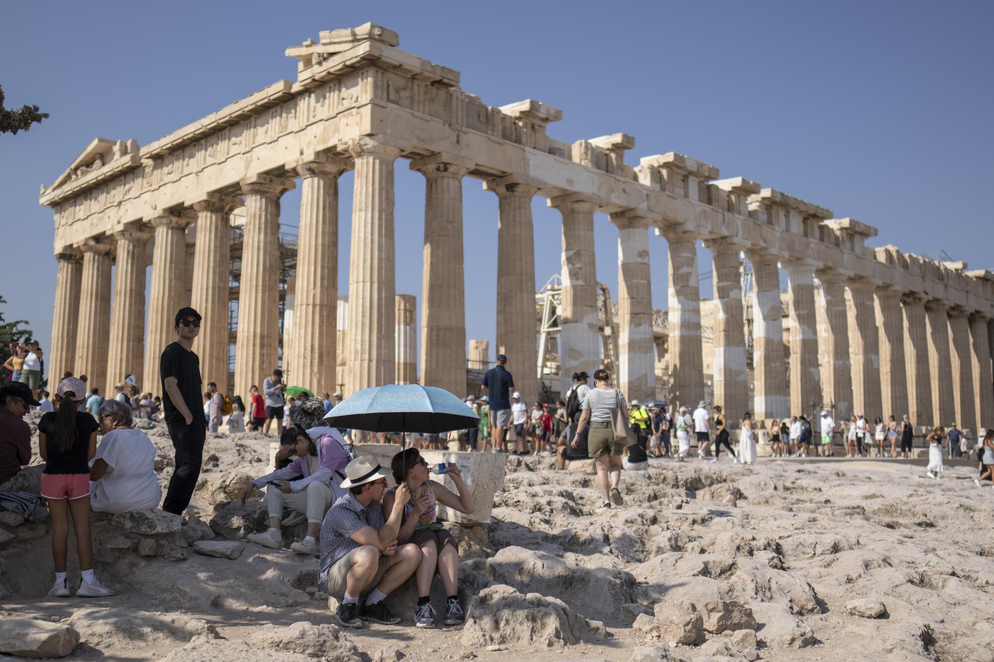 Tourists visiting the Acropolis of Athens gather around the Parthenon temple.