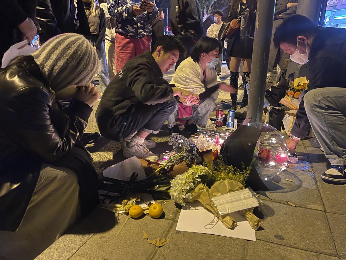 Mourners crouching beside candles and flowers on a sidewalk memorial