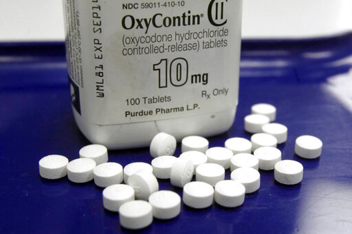 Several white pills next to an OxyContin bottle