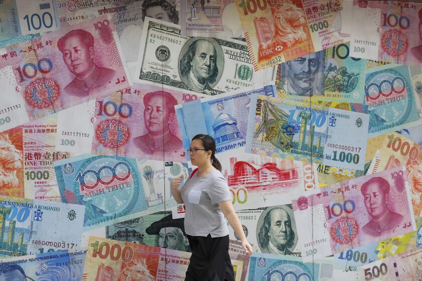 FILE - A woman walks by a money exchange shop decorated with different countries currency banknotes at Central, a business district in Hong Kong, Aug. 6, 2019. China is easing government exchange rate controls to let the Russian ruble fall faster in value against the Chinese yuan in a move that would help to insulate Beijing from economic sanctions on Moscow. (AP Photo/Kin Cheung, File)