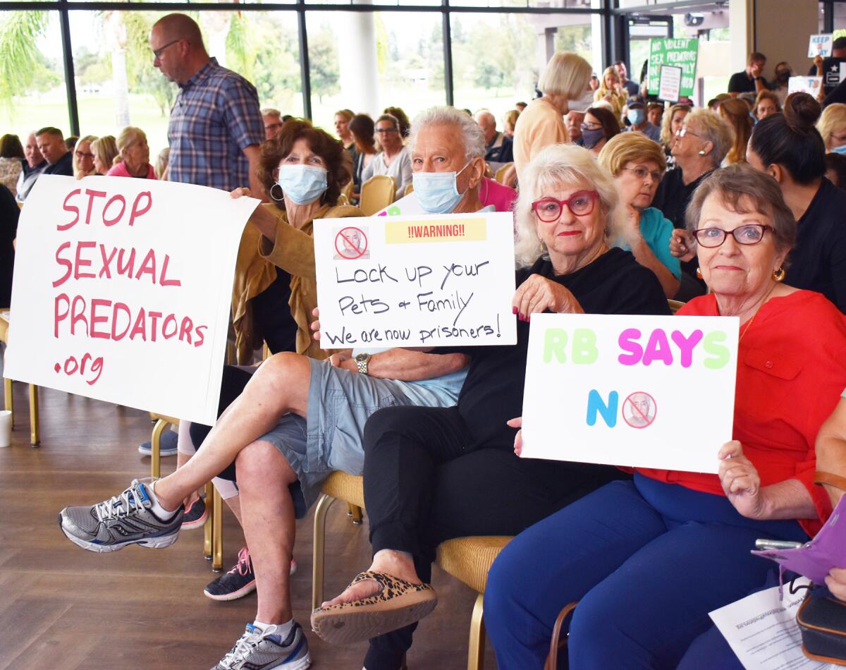 People at a meeting with signs such as "Stop sexual predators"