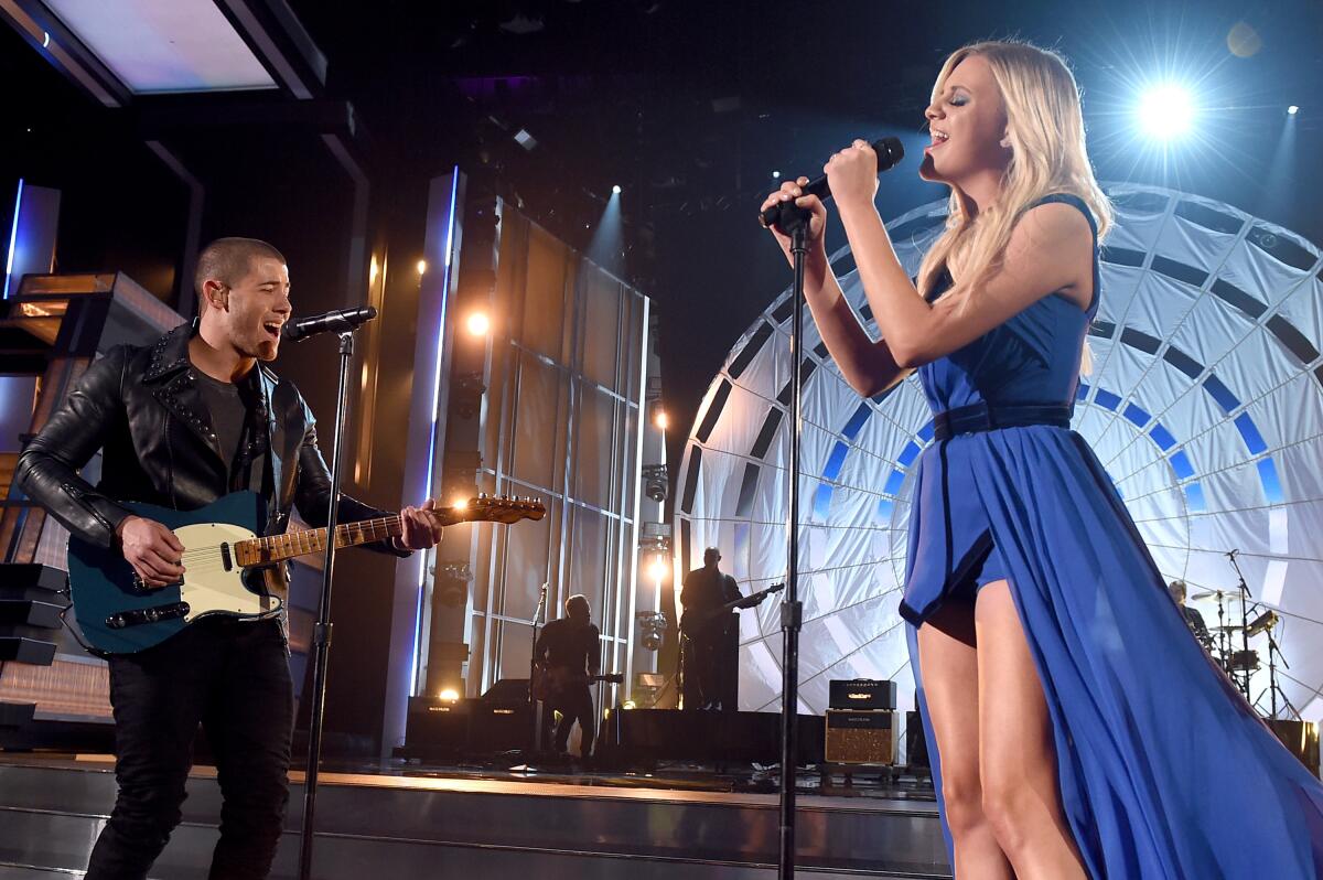 Nick Jonas plays a guitar and sings and Kelsea Ballerini also sings onstage at an awards show