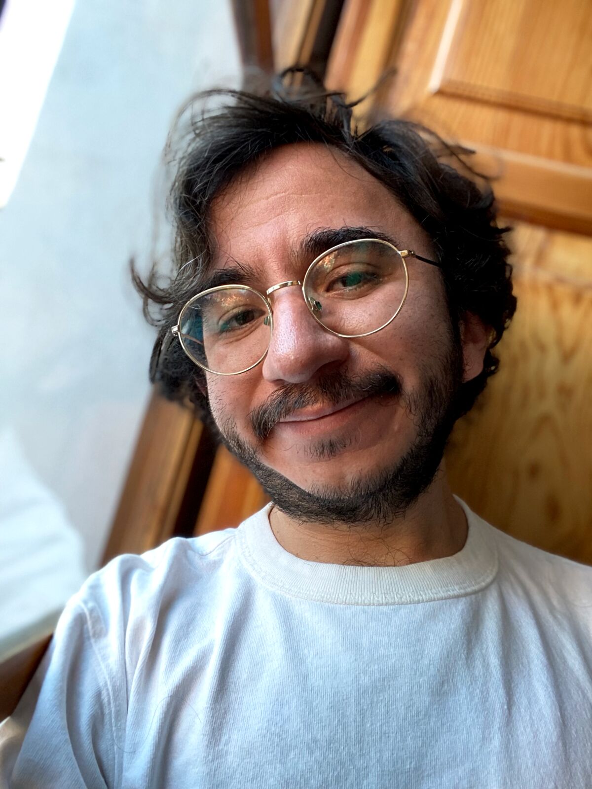 A smiling man with a beard and glasses in a light-colored shirt.