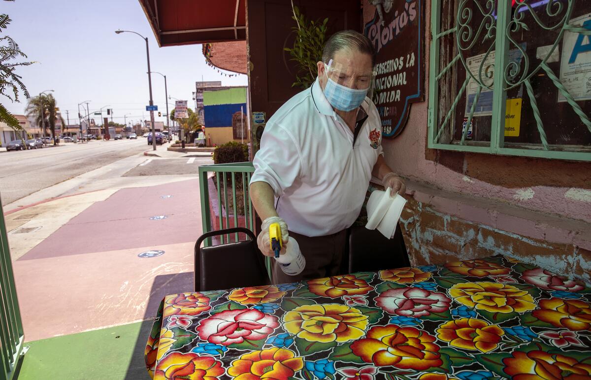 Assistant manager Luis Garcia sanitizes outdoor tables at Gloria's Restaurant in Huntington Park