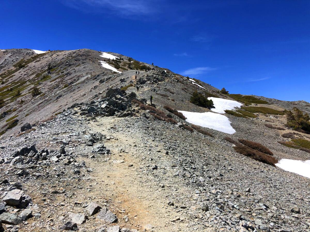 A rocky trail ascends a barren mountain ridge with patches of snow