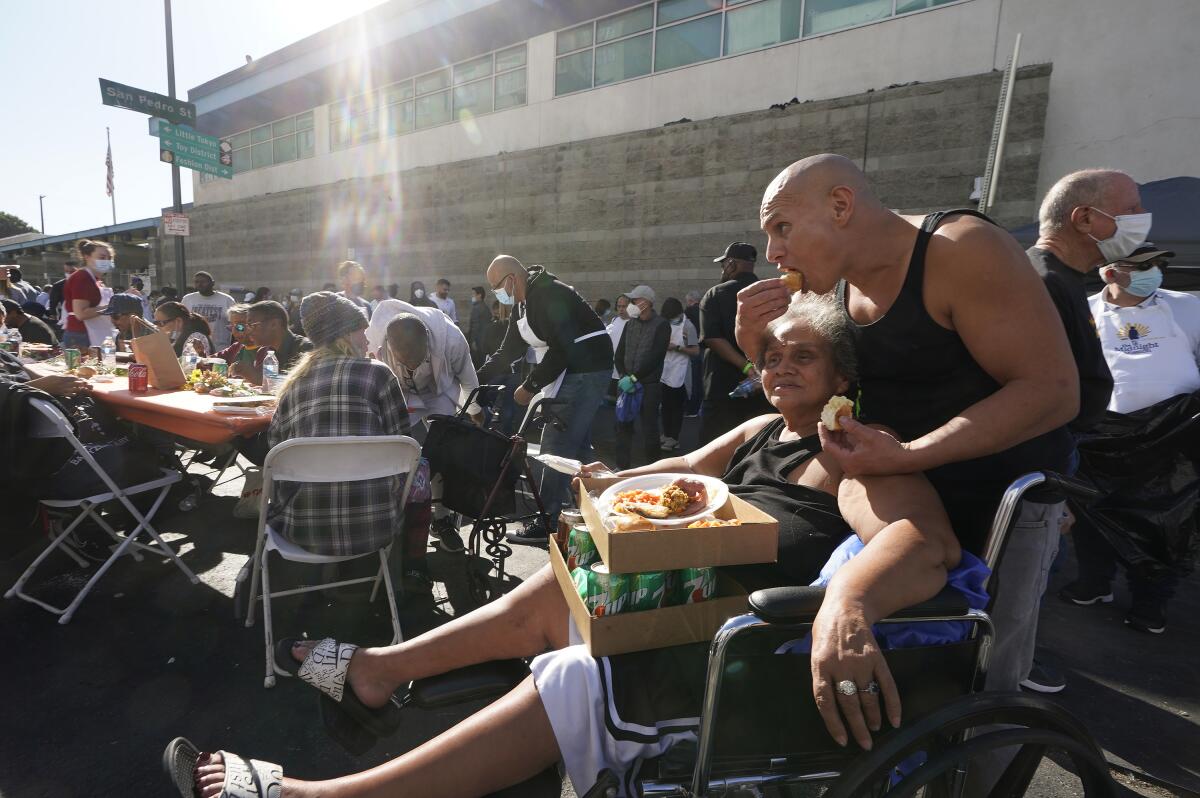 A woman in a wheelchair and a man eat Thanksgiving dinner among a large crowd outdoors